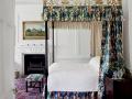 Čtyřsloupková postel zakončená zlaceným dřevěným ornamentem dominuje ložnici (Jean Monro - Clarence House).